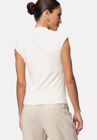 Haut ajusté blanc avec des manches courtes, une texture lisse et un ourlet droit, associé à un pantalon beige, mettant en avant un design minimaliste.