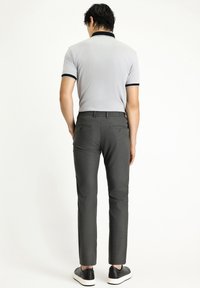 Grijze polo met korte mouwen en zwarte kraag en biezen, gecombineerd met donkergrijze maatpakken en zwarte sneakers. Focus op strakke lijnen en een moderne pasvorm.