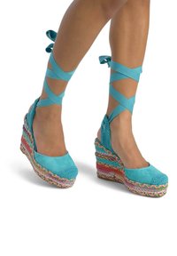 Espadrilles à talons compensés turquoise avec une semelle tissée multicolore, un design ouvert et des brides autour de la cheville. Les textures en daim et en crochet sont marquées.