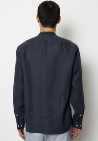 Cămașă lungă de culoare albastru închis, dintr-un material ușor, cu un croi drept, manșete cu nasturi și un design fără guler.