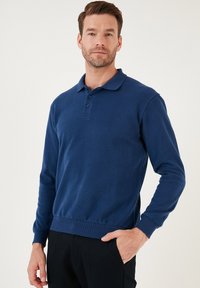 Tengerészkék, hosszú ujjú poloing, puha anyagból készült, három gombos záródással, bordás mandzsettákkal és egyenes szegéllyel.
