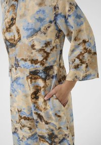 Kevyt mekko monivärisessä kuosissa, joka sisältää beigeä, sinistä ja ruskeaa sävyä. Mekossa on taskut ja kolmoneljäsosapituus hihat.