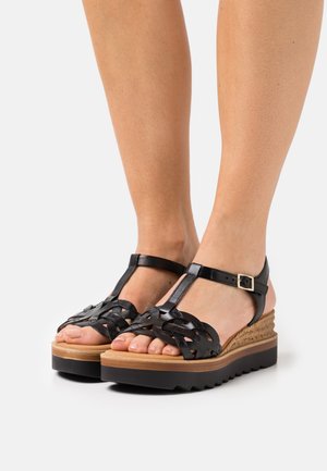 Sorte vævede sandaler med T-rem design, kork kilehæl og gummisål. Har en lille spænde og åben tå.