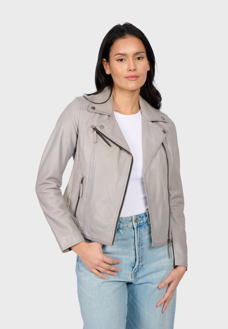 Giacca da motociclista in pelle grigia con un design aderente, spalline sulle spalle e numerosi zip. Indossata sopra una maglietta bianca e jeans in denim.