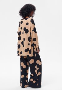 Beżowy sweter z dużymi czarnymi plamami, luźny krój, zestawiony z czarnymi spodniami ozdobionymi beżowymi wzorami w kropki. Miękki materiał i luźny fason.