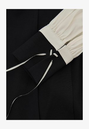 Melnas un baltas garām piedurknēm ar savākto baltu audumu, melnas aproces ar mežģīnēm melnbaltām lentām.