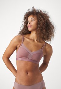 Bralette rose pâle doux avec de fines bretelles, design en V, texture lisse et détails de couture subtils. Assorti avec un bikini coordonné.