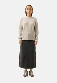 Hellgrauer strukturierter Pullover mit langen Ärmeln, kombiniert mit einem langen Jeansrock in dunkler Farbe. Akzentuiert mit lässigem Schuhwerk in gemischten Farben und Mustern.