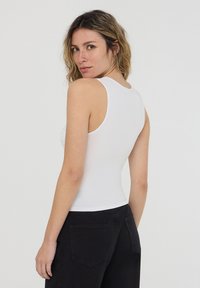Top senza maniche bianco con design aderente, caratterizzato da un scollo rotondo e una texture liscia, abbinato a pantaloni neri a vita alta.