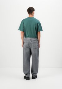 Green cotton t-shirt with a round neck, paired with loose-fit gray denim jeans featuring a classic five-pocket design and subtle texture.