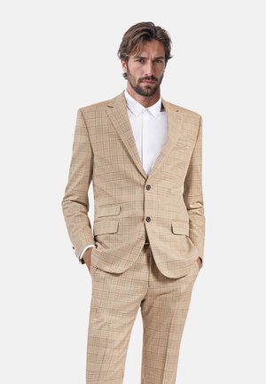 Beige karierter Anzug mit einem strukturierten Blazer und passenden Hosen. Verfügt über zwei Fronttaschen und einen Ein-Knopf-Verschluss. Weißes Hemd darunter.