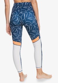 Marinblå leggings med vita bladmönster, orange detaljer och en figurnära design. Tillverkade av stretchy material, med hög midja och kontrasterande paneler.