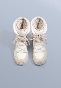 Bézs bokacsizma párnázott szárrésszel, fűzős rögzítéssel, gumitalppal és sima szövetszerkezettel. Kerek orr-résszel és redőzött díszítéssel rendelkezik.