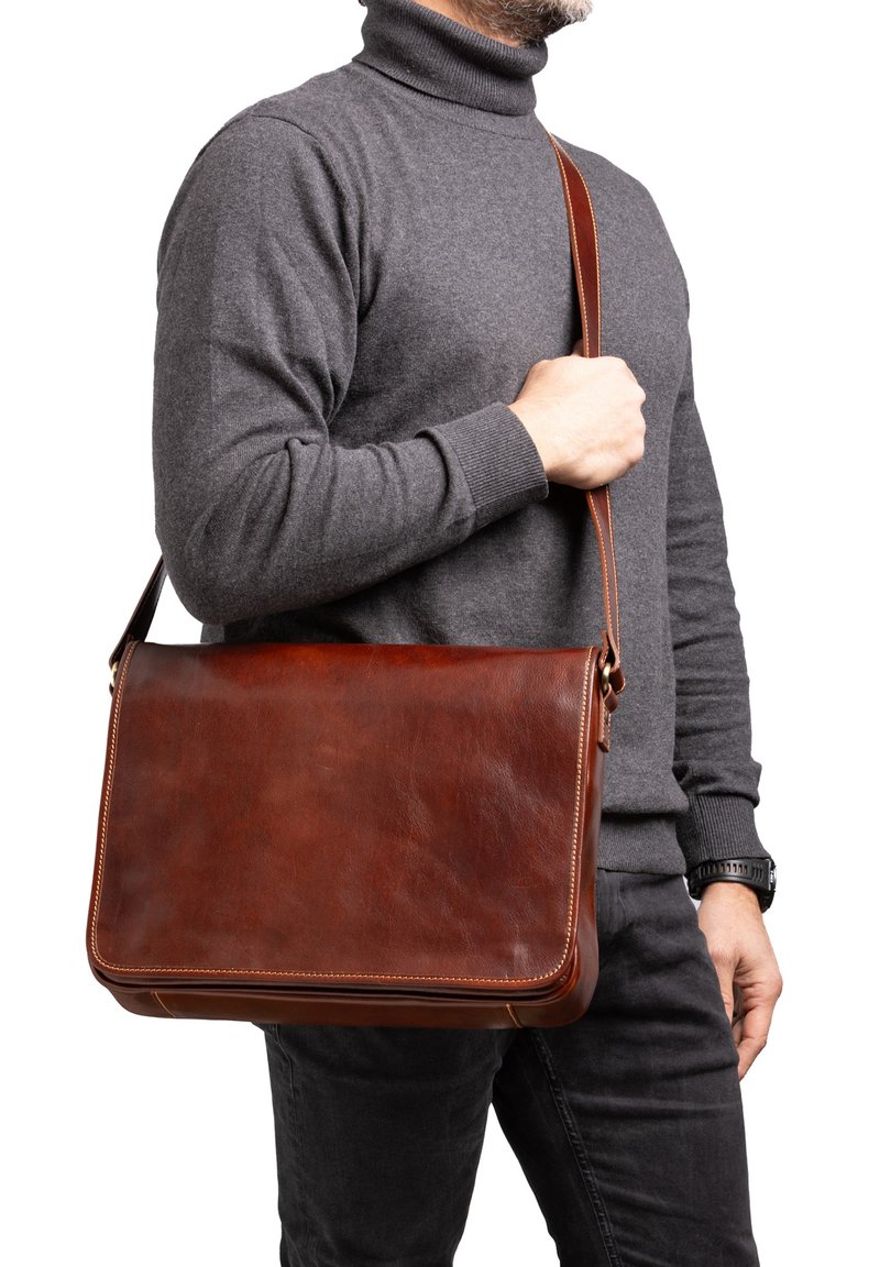 Borsa a tracolla in pelle marrone con design piatto, dettagli cuciti, tracolla regolabile e superficie liscia. Indossata da una persona su uno sfondo bianco.