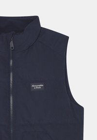 Námořnická prošívaná vesta s vysokým límcem, předním zipem a malou nášivkou loga Abercrombie & Fitch na levé straně.