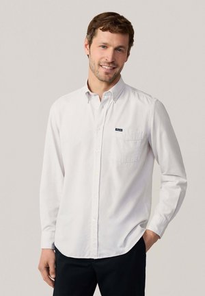 Camisa blanca de botones con cuello clásico, bolsillo frontal y etiqueta de marca sutil, hecha de tela de algodón. Mangas largas, corte relajado.