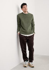 Maglione verde a maglia con orlo e polsini a coste, abbinato a pantaloni in velluto a coste marroni e scarpe da ginnastica multicolori. Design pulito e minimal.