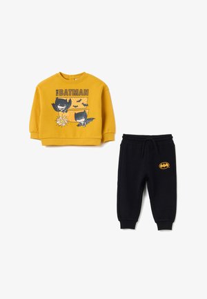 Gele sweatshirt met Batman-afbeelding en zwarte joggerbroek met een klein embleem. Zacht materiaal, casual pasvorm, elastische tailleband en boorden.