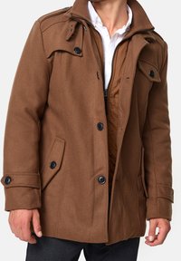 Bruine mantel van een wolmix met een rits aan de voorkant, knoopdetails en twee zijzakken. Gevoerd interieur met een subtiele doorgestikte textuur.