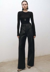 Black fitted long-sleeve top paired with high-waisted, wide-leg leather pants. Snake-print open-toe shoes. Minimalistic design with clean lines.