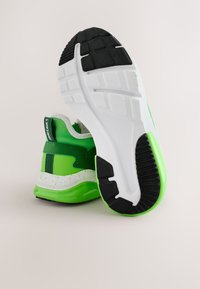 Paire de chaussures de sport vertes et blanches, l'une montrant une vue latérale, l'autre affichant la semelle noire à crampons tournée vers l'avant.