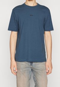 Námořnická modrá bavlněná tričko s kulatým výstřihem, krátkými rukávy a malým černým logem na hrudi. Měkká textura, volný střih.