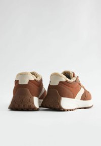 Sneaker marroni con tomaia testurizzata, accenti crema e fodera morbida. La suola è sagomata per garantire aderenza.
