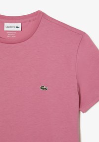 Rosa bomullströja med rund halsringning och korta ärmar. Har en liten grön broderad krokodil-logotyp på vänster bröst.