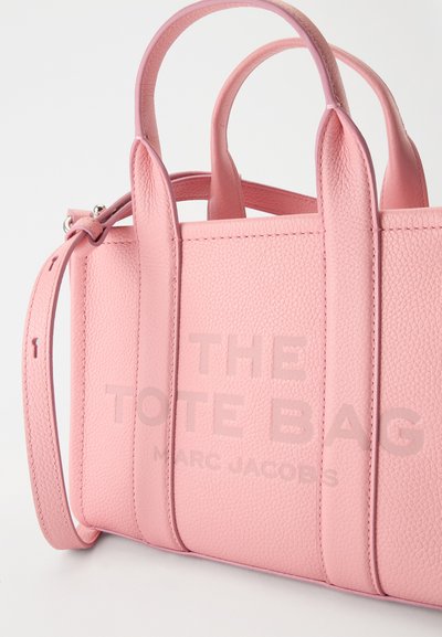 Sac cabas en cuir texturé rose avec doubles poignées supérieures, bandoulière réglable et texte embossé "THE TOTE BAG MARC JACOBS".