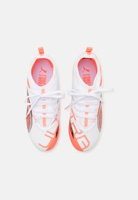 Zapatillas deportivas blancas con acentos naranjas, con parte superior de malla, letras impresas y cordones blancos. Suela texturizada con un diseño aerodinámico.