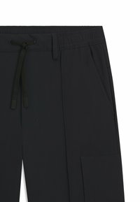 Black elastic-waist pants with contrasting drawstring, side pockets, and a smooth fabric texture; features a minimalist design without patterns.