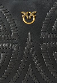 Schwarze Lederhandtasche mit aufwendiger erhabener Steppnaht und einem goldenen Hardware-Detail im Dual-Vogel-Motiv. Texturierte Oberfläche mit floralen Mustern.