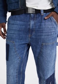 Jeans in denim con lavaggio medio, caratterizzati da sezioni in patchwork, taglio dritto e minuteria metallica sulle tasche. Con cintura in vita.