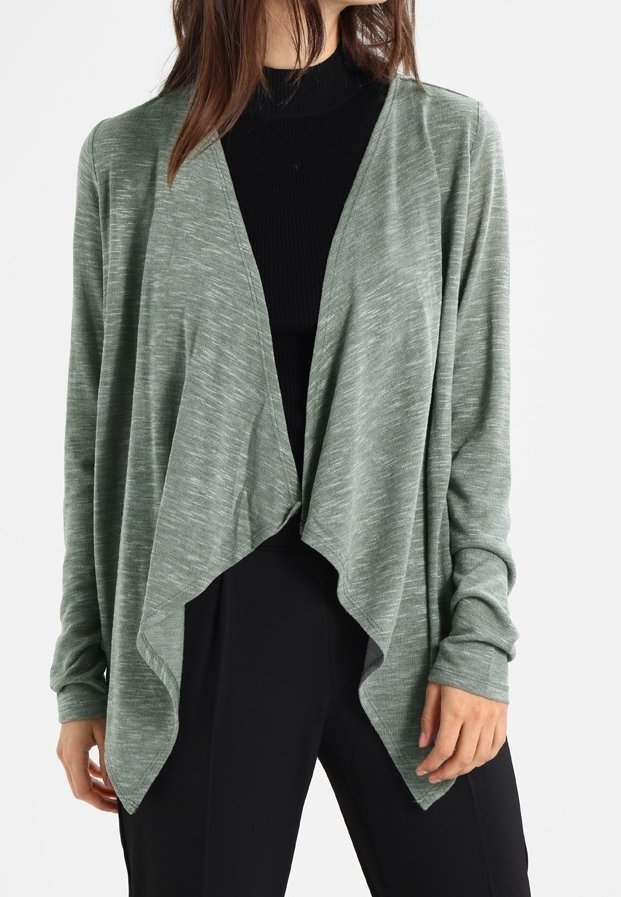 Světle zelený cardigan s volně draperovaným předním dílem, dlouhými rukávy a měkkou texturou. Nositý přes černý rolák, se volným střihem.
