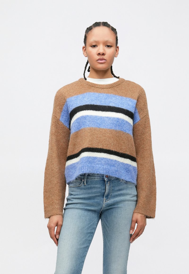 Pulover maro tricotat cu dungi albastre, negre și albe. Design scurt, croială lejeră și guler răsucit. Asortat cu blugi deschiși la culoare.