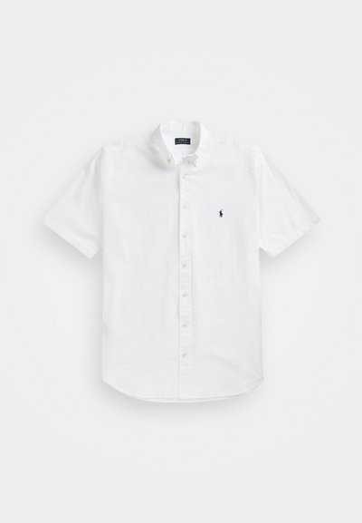 Hvitt kortermet skjorte med knappestolpe og en liten marineblå logo på brystet, har klassisk krage og rett kant. Lettvektig stoff.