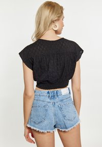 Bluză neagră texturată, scurtă, cu mâneci tip cap și tiv plisat, asortată cu pantaloni scurți din denim albastru deschis, cu margini destrămate și buzunare la spate.