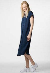 Marineblaues knielanges Kleid aus glattem Stoff mit kurzen Ärmeln, V-Ausschnitt und seitlichen Schlitzen, kombiniert mit weißen Sneakers.