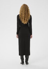 Juodas ilgas rankovinis suknelė tiesia siluetu, pagaminta iš lygaus audinio, siekianti iki pusės blauzdų, derinama su juodais batais iki kelių.