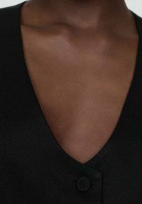 Gilet nero con profondo scollo a V e chiusura con un singolo bottone, realizzato in un tessuto morbido, che mette in risalto un design minimalista.