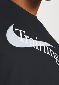 Primer plano de una camiseta negra con el texto blanco "Entrenamiento" y un gráfico de línea gris claro que cruza el pecho.
