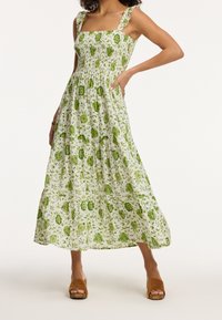 Maxikleid in Weiß mit grünem Blumenmuster. Verfügt über einen quadratischen Ausschnitt, ein gerafftes Oberteil und Rüscheträger. Aus glattem, leichtem Stoff.