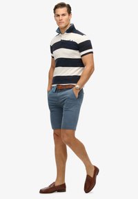 Polo a righe navy e bianche con colletto, abbinato a pantaloni corti blu. Una cintura in pelle marrone e mocassini completano l'outfit.
