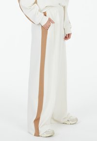 Wide-leg pants in cream with a contrasting brown side stripe. Features an elastic waistband and side pockets. Made of soft fabric.