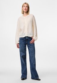 Light beige, fuzzy cardigan with a round neck and five button front, paired with dark blue wide-leg jeans featuring a classic denim texture.