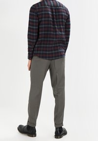 Langarm geruite shirts in marineblauw, bordeauxrood en groen, gecombineerd met lichtgrijze, taps toelopende broeken en zwarte enkellaarsjes. Platte achterkant ontwerp.