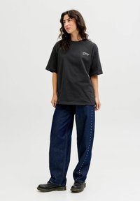 Sort bomulds T-shirt med korte ærmer og et logo på brystet, parret med brede jeans i blå farve med sidelommer og sorte støvler.