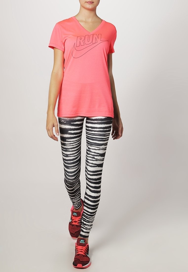 T-shirt rose vif à col en V avec l'inscription "RUN" en texte foncé, assorti à des leggings zébrés noir et blanc et des chaussures de sport rouges.