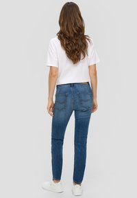 Jeans de mezclilla ajustados de color azul con una cintura de altura media, cuatro bolsillos y costuras en contraste, llevados con una camiseta blanca y zapatillas blancas.