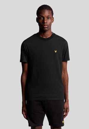 Svart bomulls t-shirt med rund halsringning, korta ärmar och en liten gul örnlogo på vänster bröst. Slät struktur och figurnära passform.